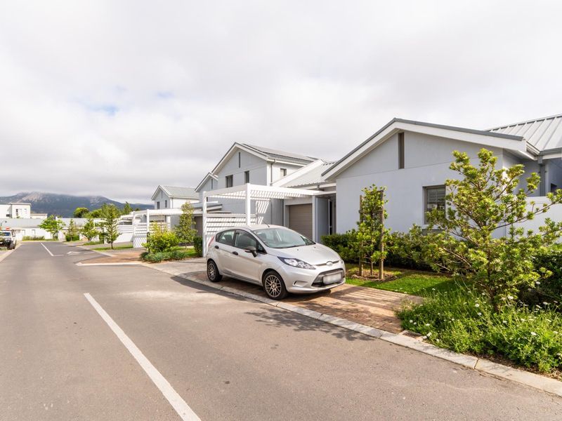 A street-level view of a modern residential estate featuring contemporary homes with metal roofs, paved driveways, and integrated pergolas.