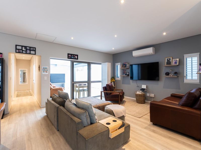 A well-maintained living room featuring laminate flooring, recessed lighting, a split-system air conditioner, and large aluminium sliding doors leading to an outdoor area.