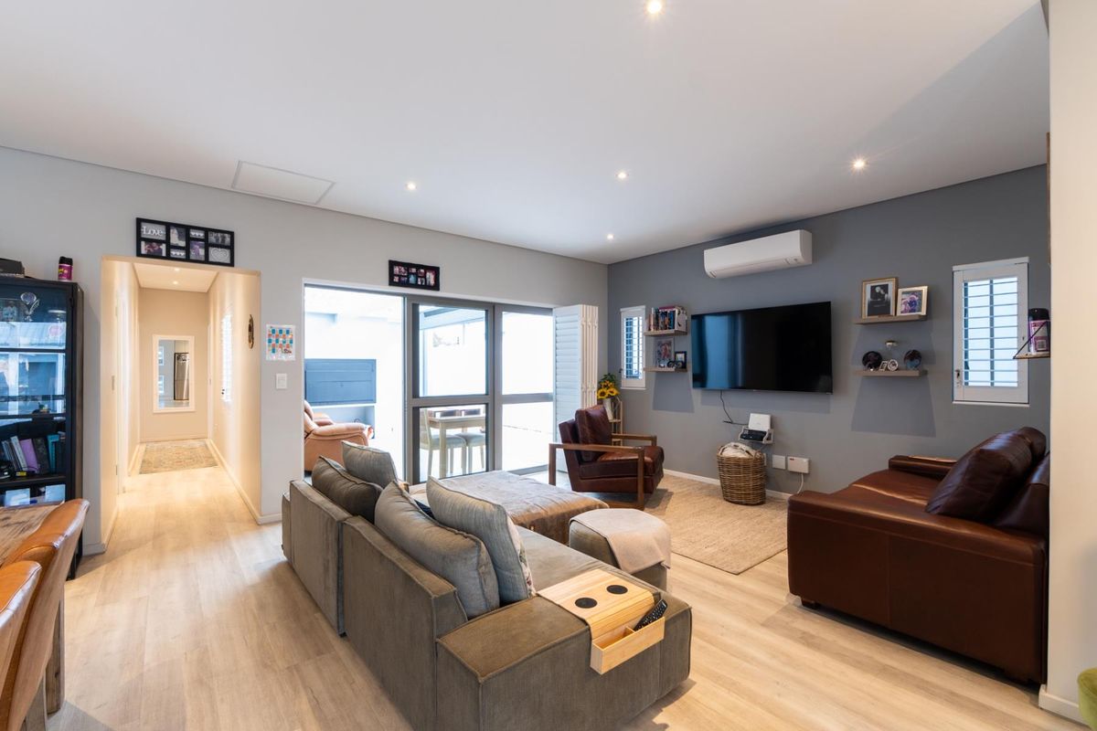 A well-maintained living room featuring laminate flooring, recessed lighting, a split-system air conditioner, and large aluminium sliding doors leading to an outdoor area.