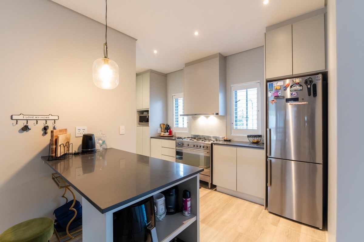 Modern kitchen featuring stone countertops, gas hob, extractor fan, built-in oven, and ample cabinetry with integrated lighting and shutter blinds.