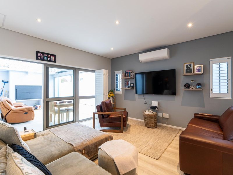 A well-maintained living room featuring laminate flooring, recessed lighting, a split-system air conditioner, and large sliding doors providing access to the patio.
