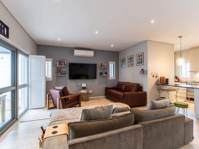 A bright open-plan living and kitchen area featuring modern laminate flooring, recessed lighting, split-system air conditioning, and seamless access to the outdoor patio.