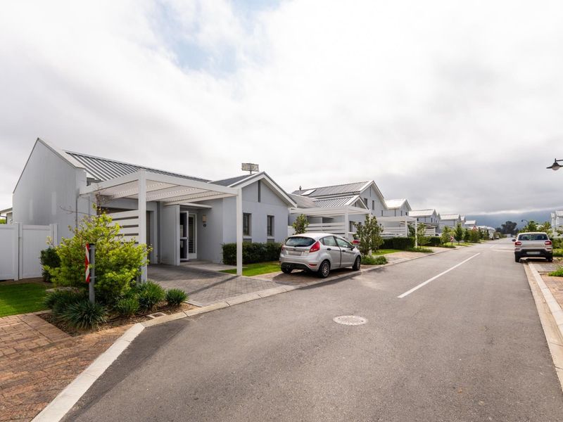 A street view of a residential estate featuring modern single-story homes with metal roofs, paved driveways, and attached pergolas.