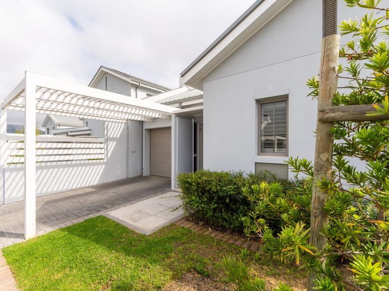 Front exterior view of the property featuring a paved driveway, a white pergola structure, and a well-maintained garden area leading to the garage.