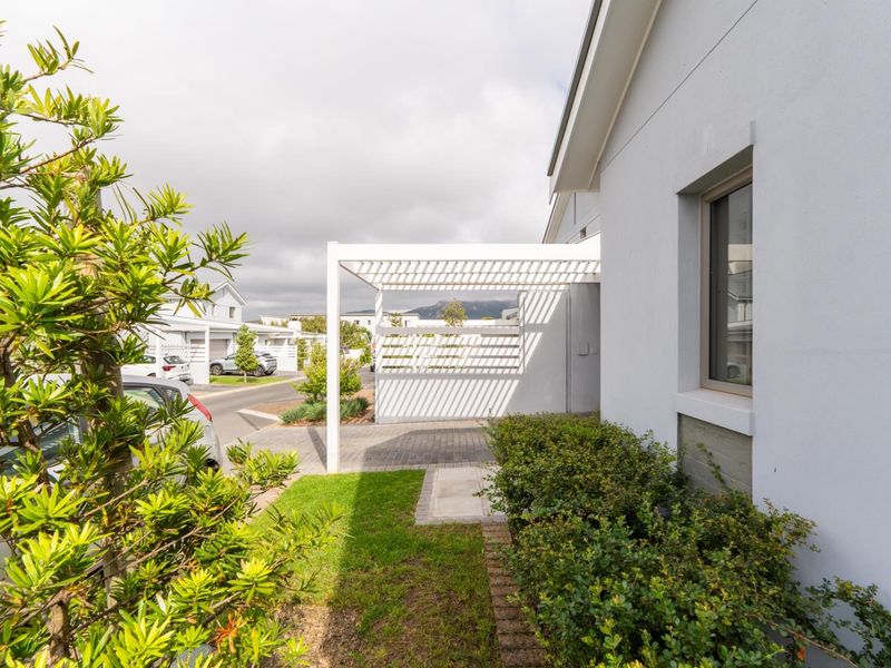 Front exterior view featuring a modern white pergola, paved driveway, and well-maintained garden area.