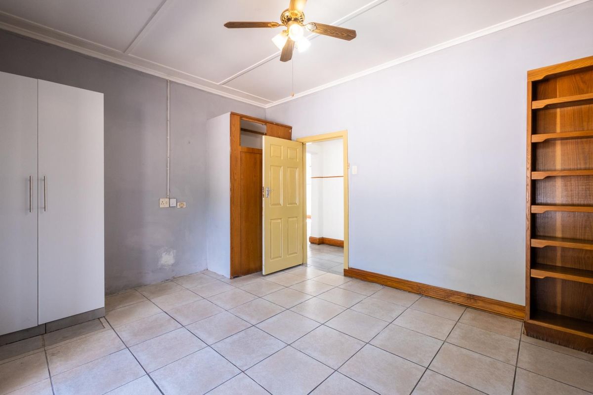 An empty bedroom featuring tiled flooring, a ceiling fan, and built-in storage, requiring minor cosmetic repairs to the wall surfaces.