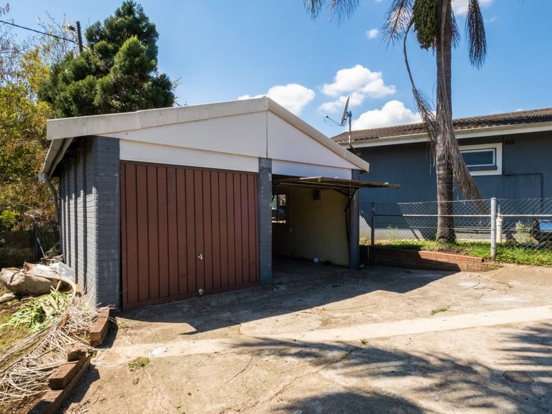 A detached double garage featuring brick construction and a concrete driveway, showing signs of wear and requiring maintenance to the door and exterior finishes.