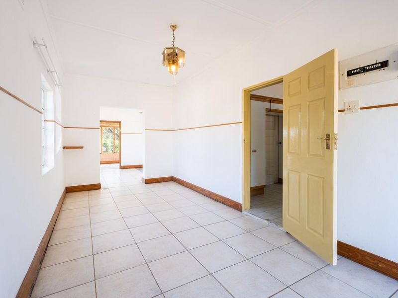 A bright, empty living area featuring neutral tiled flooring, timber trim details, and a functional electrical distribution board.