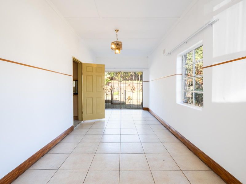 A bright, empty living area featuring tiled flooring, a security gate leading to the exterior, and natural light through a side window.