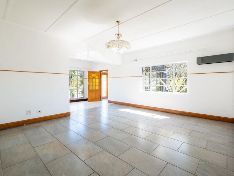 A bright and spacious living area featuring neutral tiled flooring, large windows, and an installed air conditioning unit, offering a clean and versatile living space.