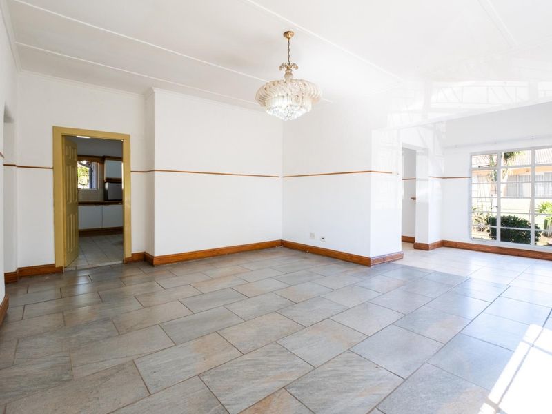 A bright and spacious living area featuring neutral tiled flooring, a decorative crystal chandelier, and classic wooden trim details throughout.