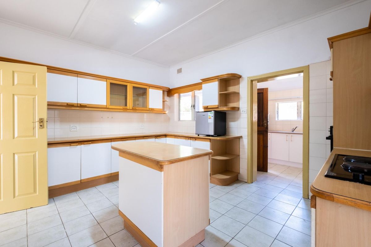 A functional kitchen featuring built-in cabinetry, a central island, tiled flooring, and a tiled backsplash, with direct access to an adjoining scullery area.
