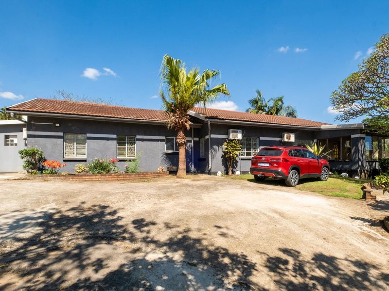 Front elevation of a single-story house featuring a tiled roof, security bars on windows, and a large concrete driveway area.