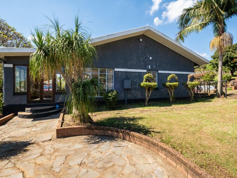 Rear exterior view of the house featuring a stone paved patio, brick retaining wall, and established garden area with mature trees.