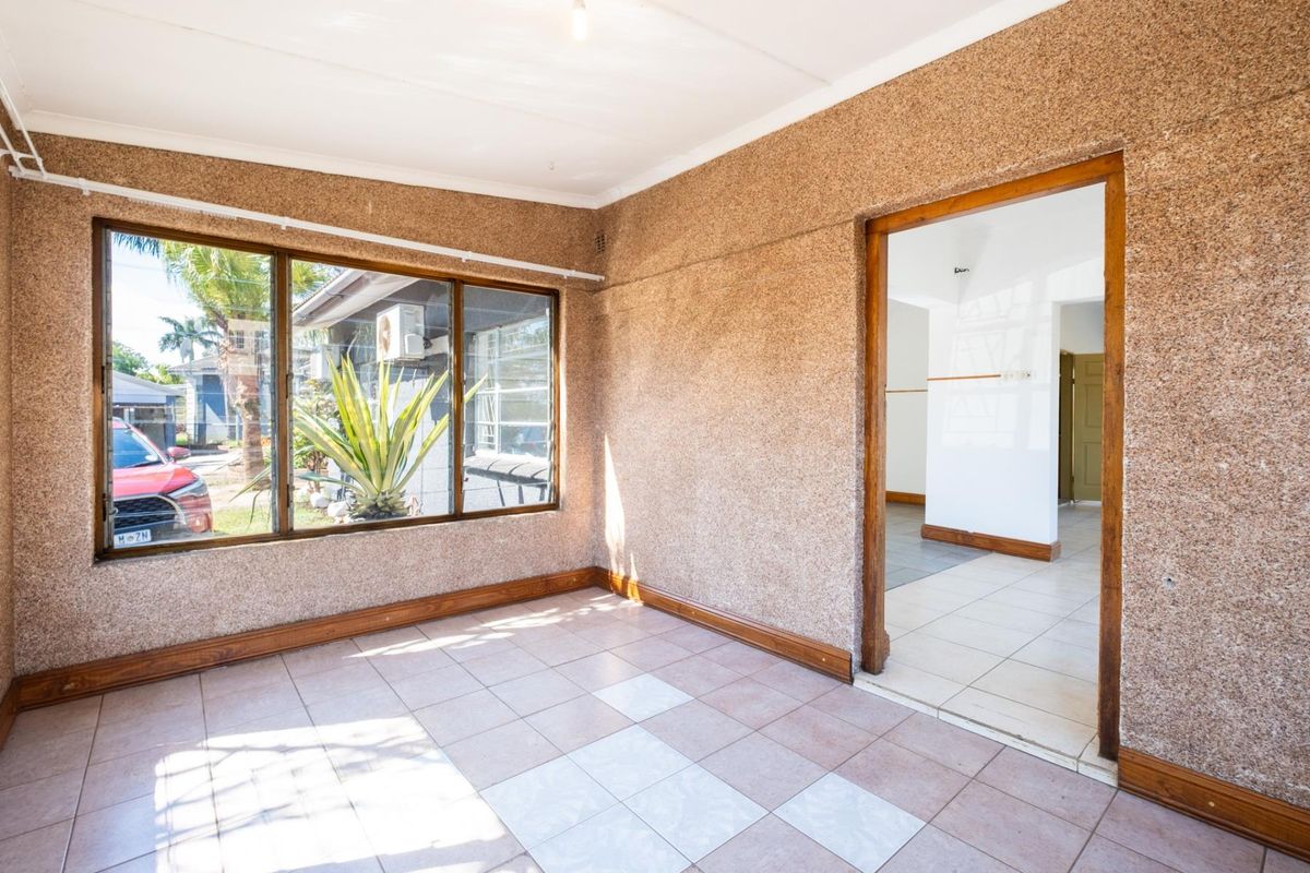 An empty living area featuring textured walls, tiled flooring, and timber door and window frames, offering a blank canvas for renovation.