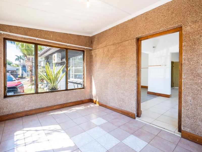 An empty living area featuring textured walls, tiled flooring, and timber door and window frames, offering a blank canvas for renovation.