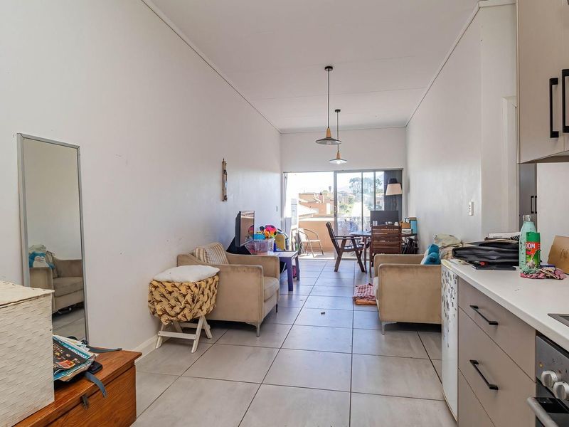 Open-plan living and kitchen area featuring tiled floors, modern cabinetry, built-in appliances, and direct access to a balcony.