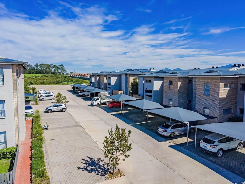 Aerial view of the apartment complex featuring paved parking areas, covered carports, and modern brick and plaster building facades.