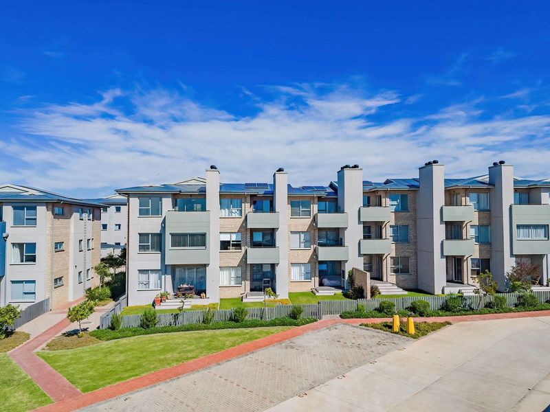 A clear aerial view of a modern apartment complex featuring brick facades, private balconies, solar panels, and well-maintained communal lawn areas.