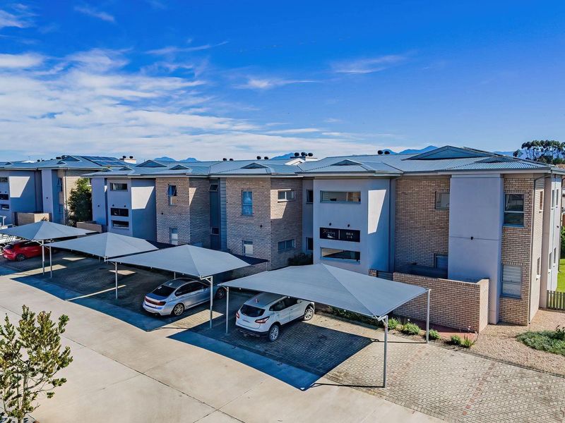Aerial view of a modern apartment complex featuring brick and rendered facades, metal roofing, and dedicated covered parking bays for residents.