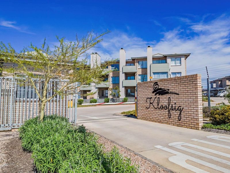 The entrance to Kloofsig apartment complex featuring a secure gated access point, brick boundary wall, and well-maintained paved driveway.