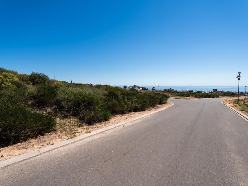 A view of the paved street and curbing leading towards the residential land, featuring coastal views in the distance.