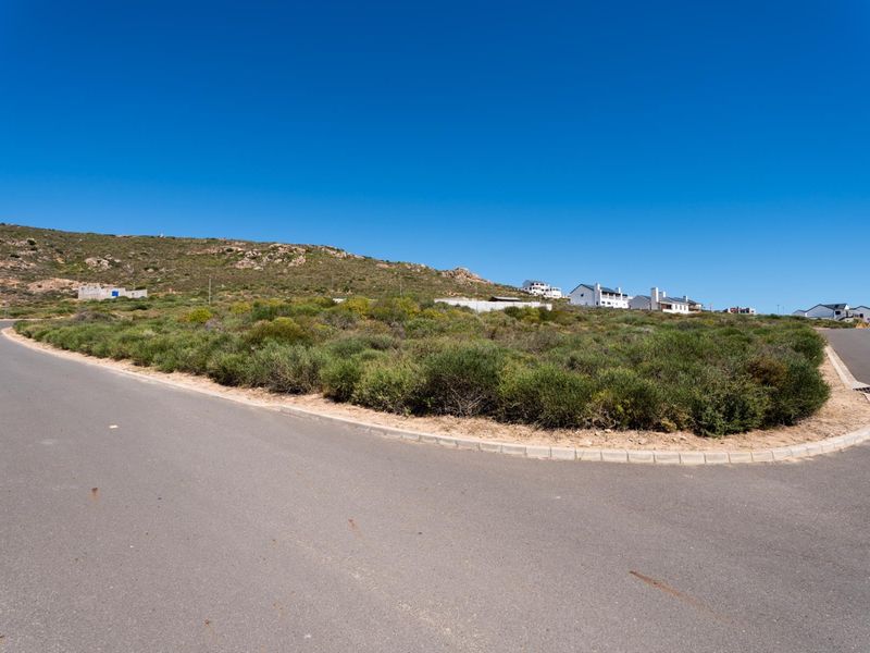 A view of a vacant residential plot situated on a corner lot with established road infrastructure and native coastal vegetation.