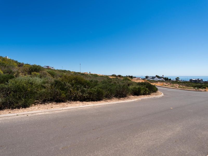 A view of the paved street frontage and concrete curbing bordering the vacant residential land with coastal views in the distance.