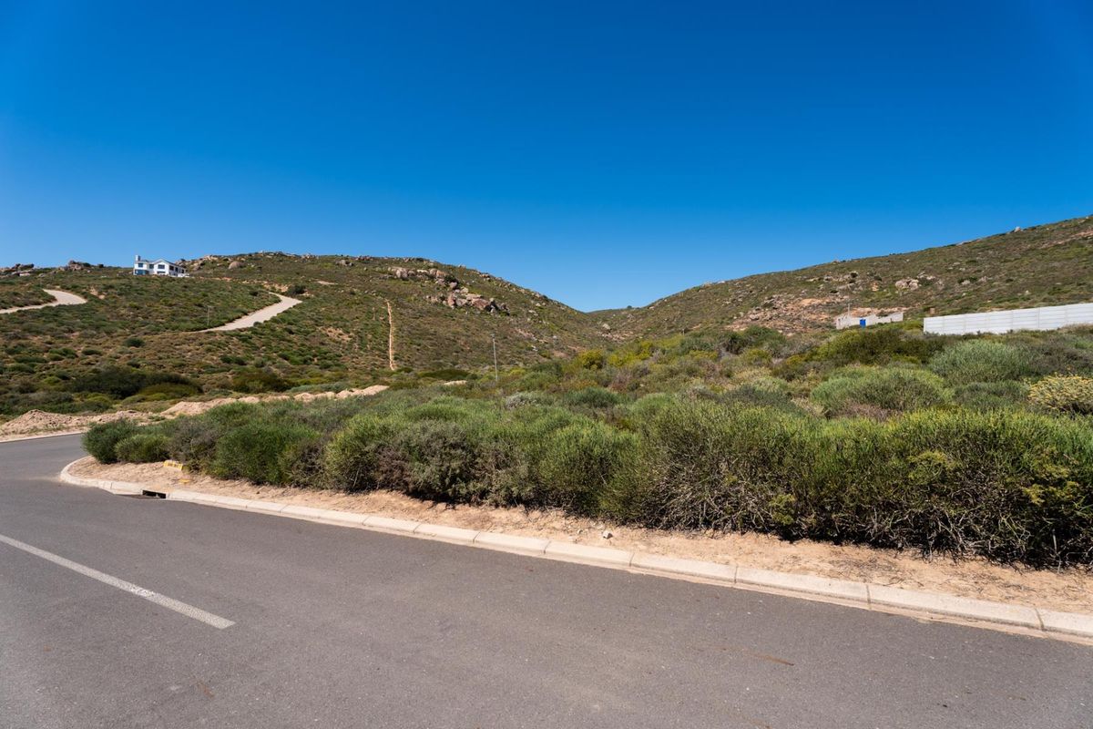 A view of the paved street and concrete curbing bordering the vacant residential land, featuring natural hillside terrain and surrounding landscape.