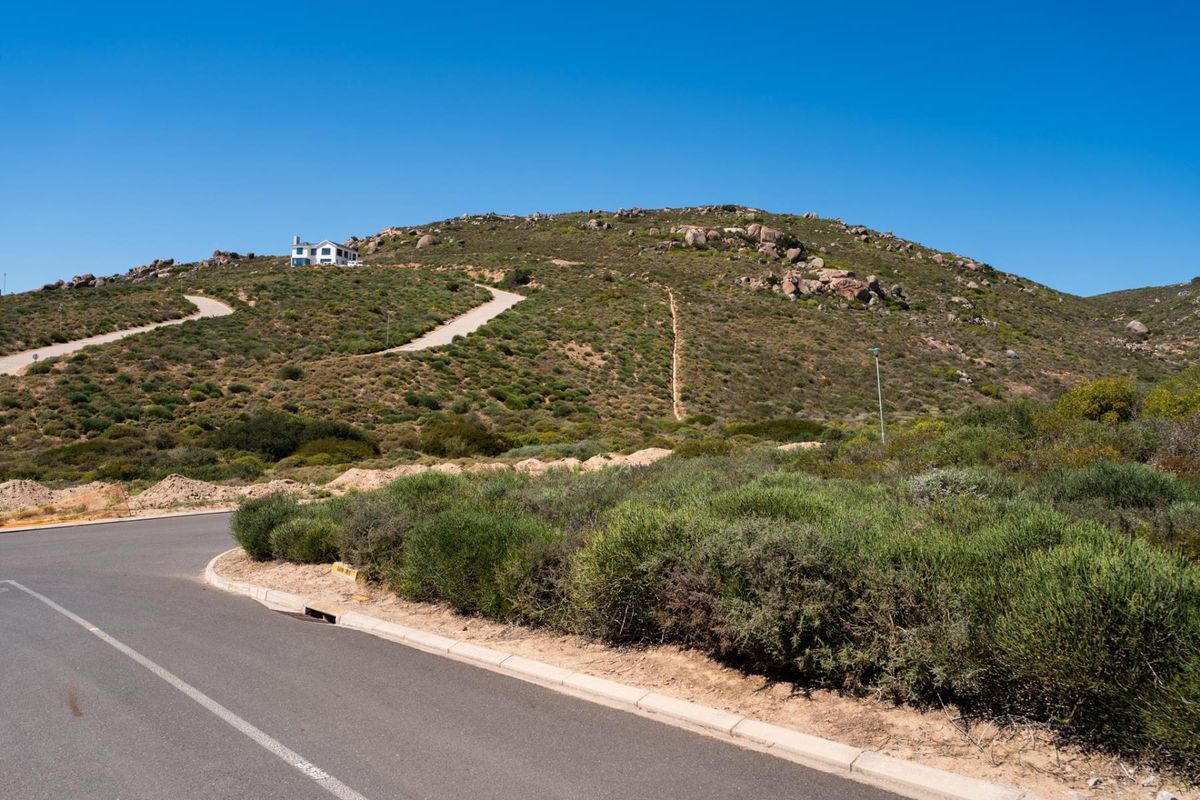 A view of the paved street and curb infrastructure leading towards the elevated hillside residential plot.