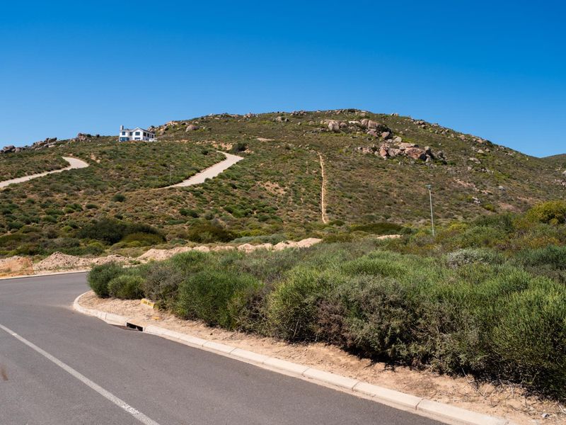 A view of the paved street and curb infrastructure leading towards the elevated hillside residential plot.