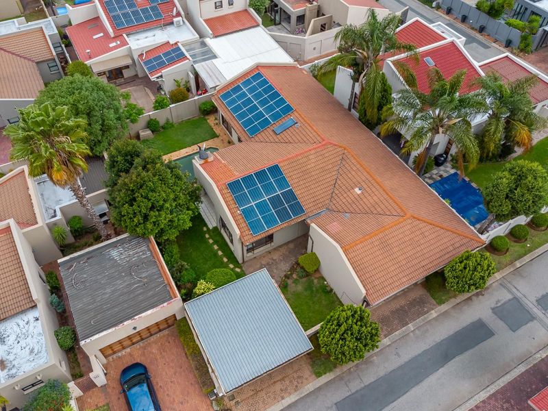 Aerial view of a residential property featuring a tiled roof with solar panels, a swimming pool, a paved driveway, and a garage.