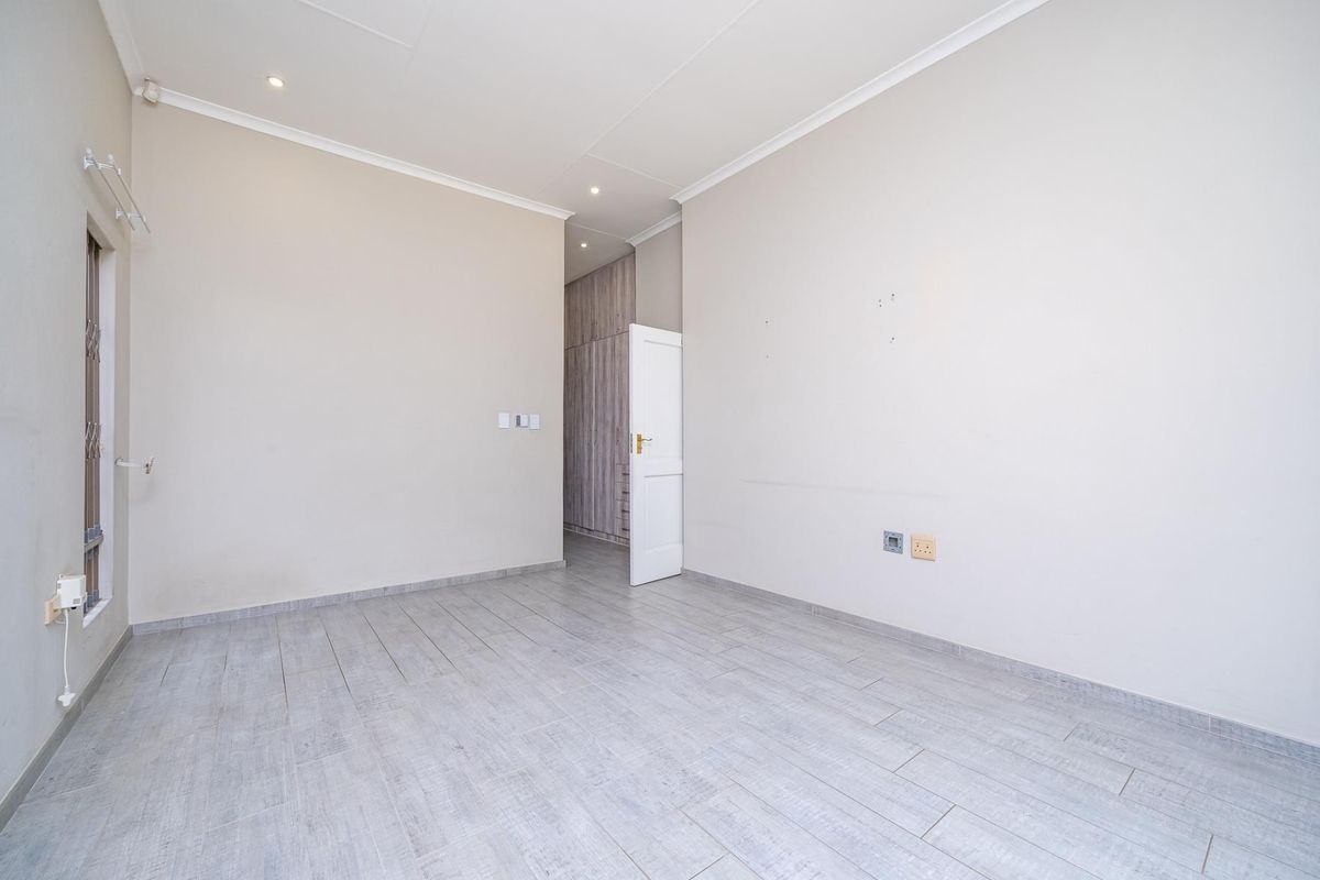 A bright, empty bedroom featuring modern tiled flooring, recessed downlights, and built-in cupboards, offering a clean and neutral space ready for personalization.