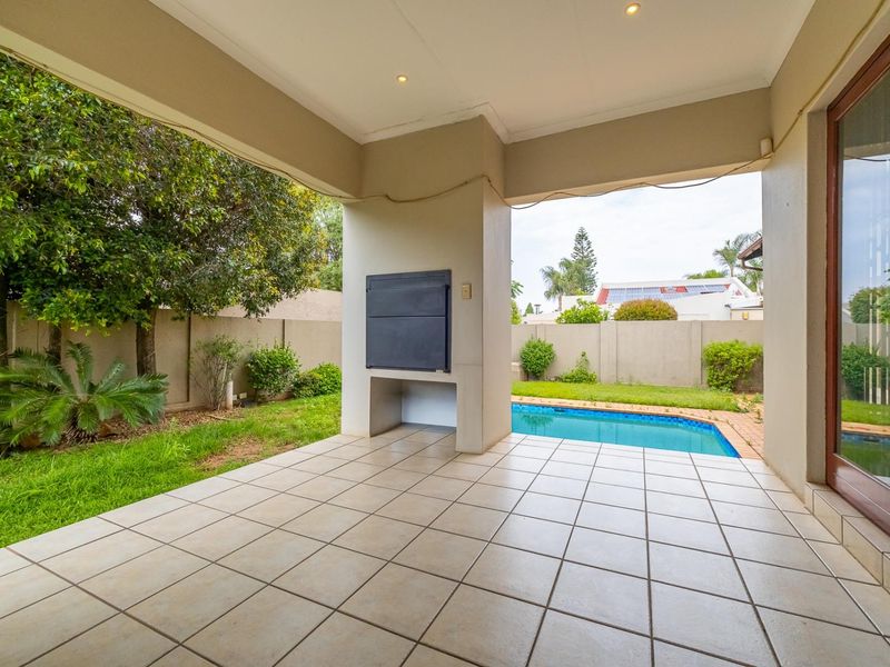 Covered patio featuring a built-in braai, tiled flooring, and direct access to the swimming pool and garden area.