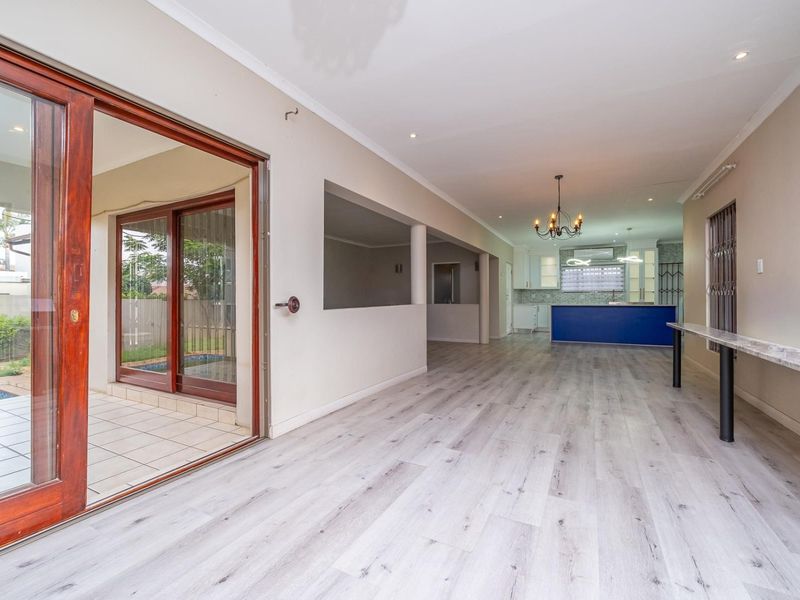 Spacious open-plan living area featuring modern laminate flooring, sliding doors to the patio, and a contemporary kitchen with a central island.