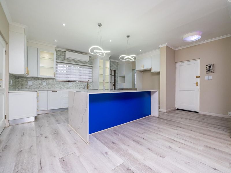 Modern, bright kitchen featuring a central island with a bold blue accent, white cabinetry, quartz countertops, and light-toned laminate flooring.