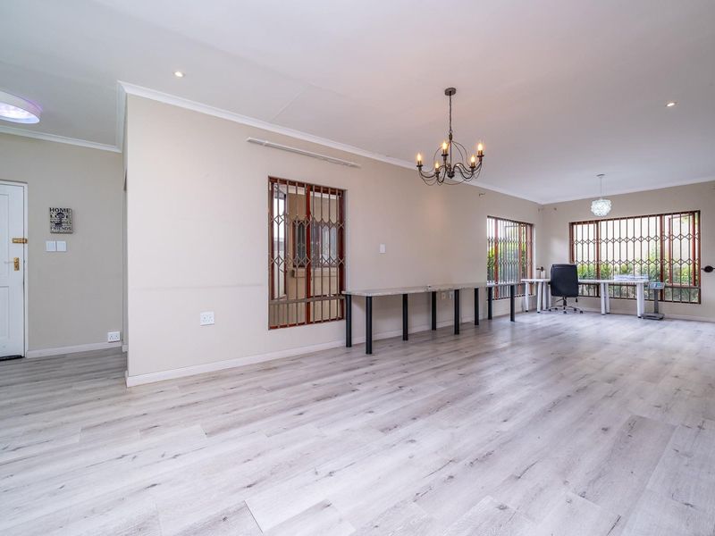 Spacious living area featuring light-toned laminate flooring, security gates on windows, and modern lighting fixtures, offering a versatile open-plan layout.