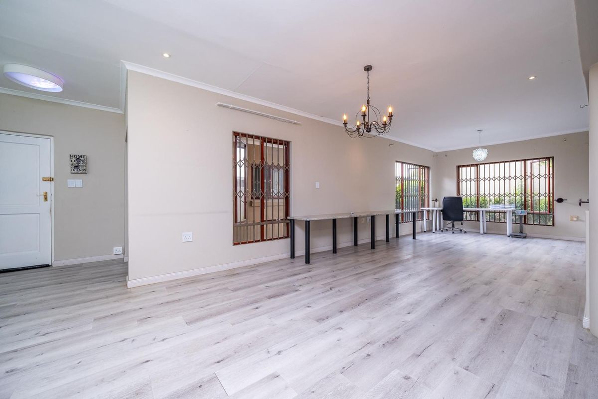 Spacious living area featuring light-toned laminate flooring, security gates on windows, and modern lighting fixtures, offering a versatile open-plan layout.