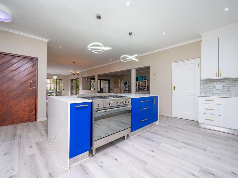 Modern open-plan kitchen featuring a vibrant blue island with a gas stove, marble-look countertops, subway tile backsplash, and light wood-look laminate flooring.