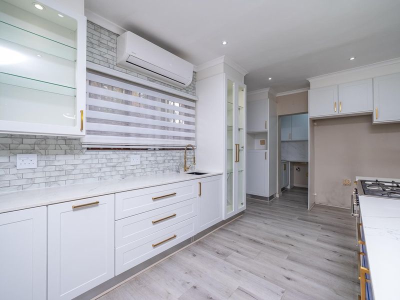 Modern kitchen featuring white cabinetry, marble-look backsplash, quartz countertops, gas hob, and integrated display cabinets with high-quality finishes.