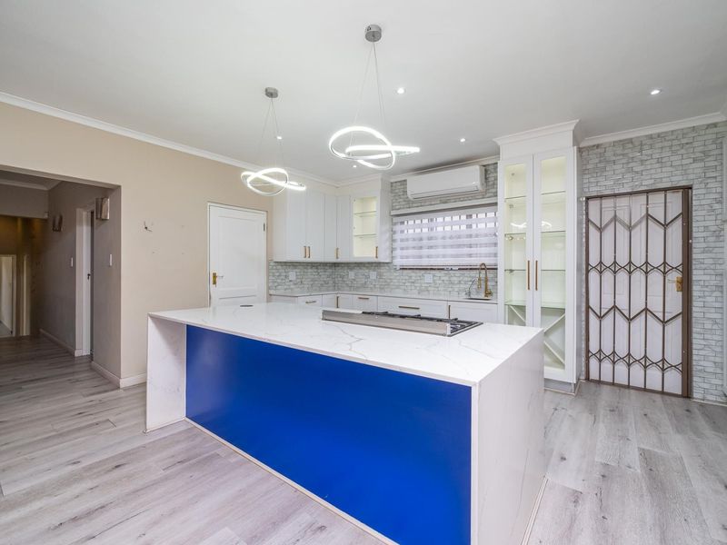 Modern kitchen featuring a central island with a stone countertop, built-in gas hob, white cabinetry, glass-front display units, and stylish pendant lighting.