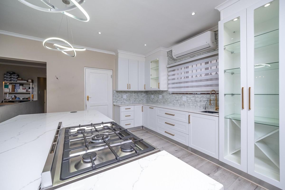 Modern kitchen featuring white cabinetry, quartz countertops, a gas hob, subway tile backsplash, and integrated glass display shelving with contemporary lighting.