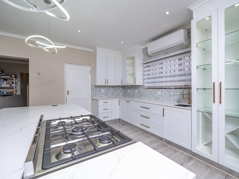 Modern kitchen featuring white cabinetry, quartz countertops, a gas hob, subway tile backsplash, and integrated glass display shelving with contemporary lighting.