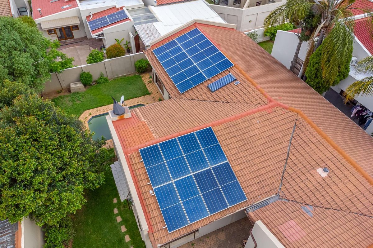 Aerial view of the property featuring a tiled roof equipped with solar panels and a solar water heater, overlooking a private garden and pool.