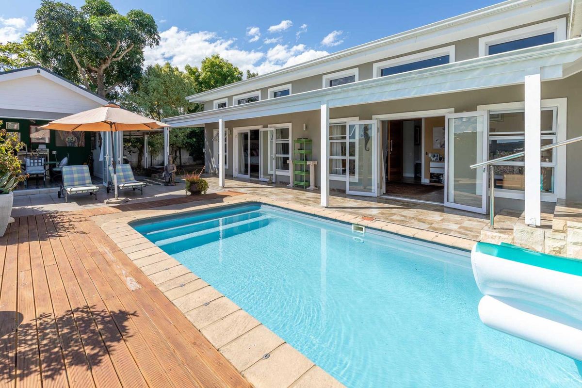 A well-maintained outdoor pool area featuring a swimming pool, timber decking, and a covered patio with direct access to the home via glass doors.