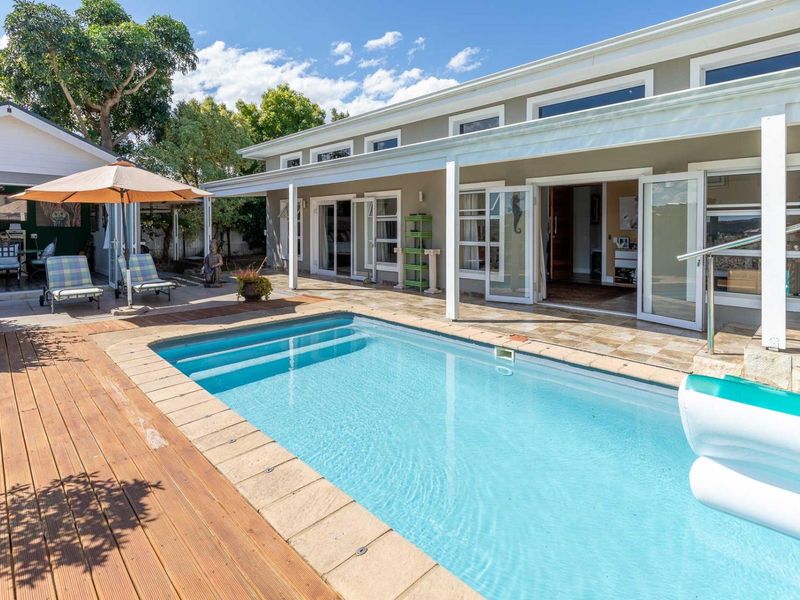 A well-maintained outdoor pool area featuring a swimming pool, timber decking, and a covered patio with direct access to the home via glass doors.