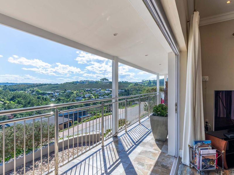 A spacious covered balcony featuring a stainless steel balustrade, tiled flooring, and expansive views of the surrounding landscape.