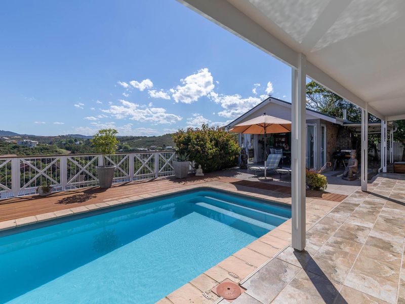 A well-maintained outdoor pool area featuring a timber deck, tiled patio, and covered veranda with scenic hillside views.