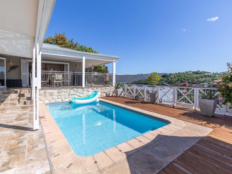 Outdoor pool area featuring timber decking, stone-clad retaining wall, and a covered patio with scenic views.