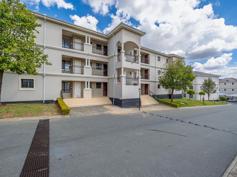 A well-maintained multi-story apartment complex featuring paved entrances, private balconies with metal railings, and landscaped surroundings.